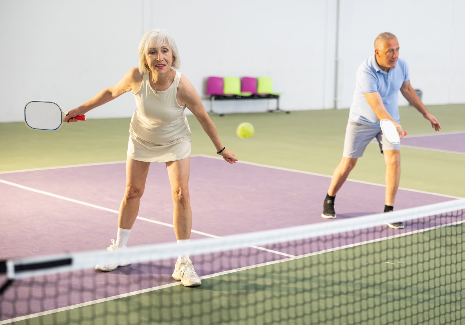 Two older adults playing pickleball
